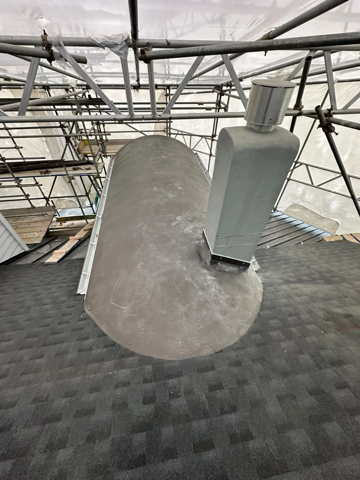 Flue penetration flashed into a shingle roof beside a barrel roof element
